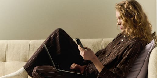 A woman with curly hair looking at her smartphone outdoors on a city street.