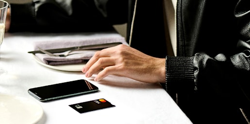 Hands holding a green credit card and smartphone, with a laptop on a desk.