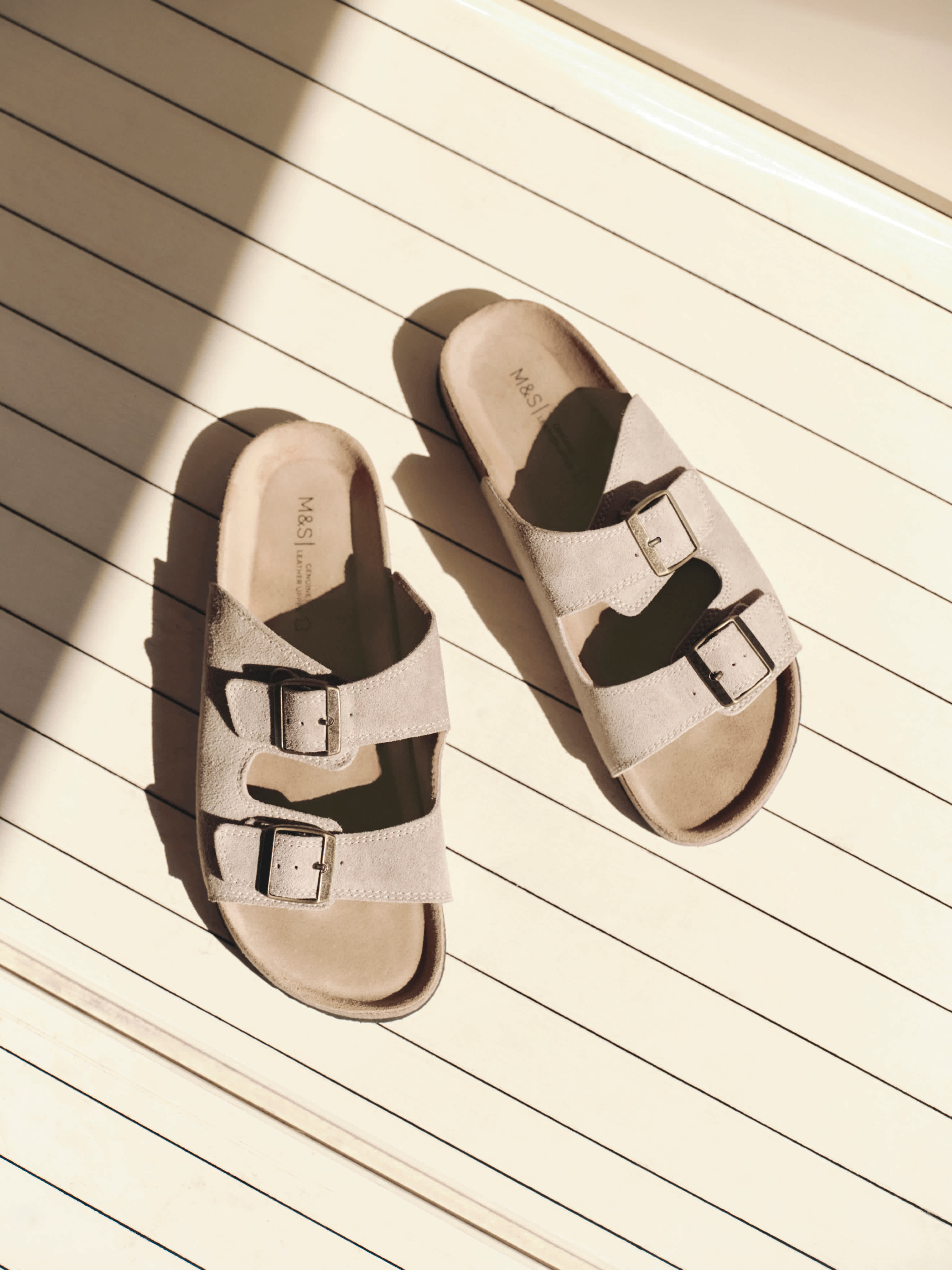 Pair of beige sandals with double buckle straps on wooden deck