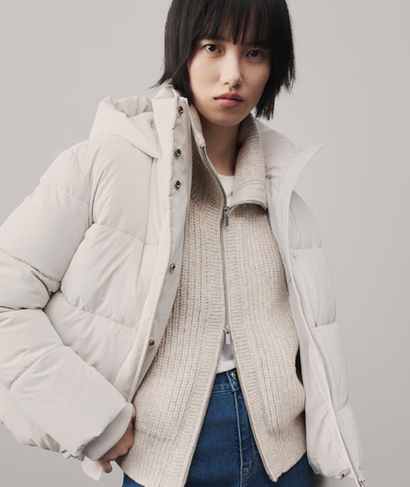 Woman wearing a cream puffer jacket. Shop women’s everyday essentials