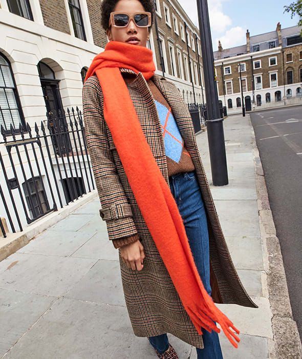 Woman wearing tweed coat, jeans and orange scarf. Shop women’s new-in.