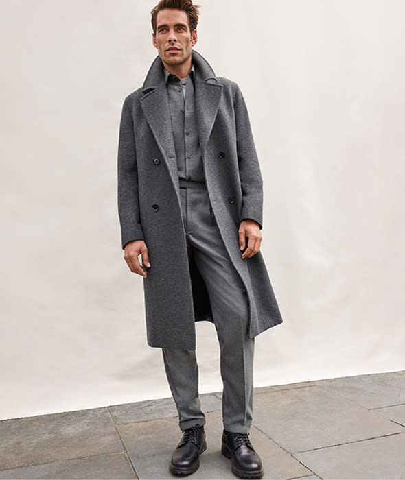 Man wearing ‘groutfit’ consisting of grey overcoat, grey flannel shirt, grey tailored trousers and black leather shoes.