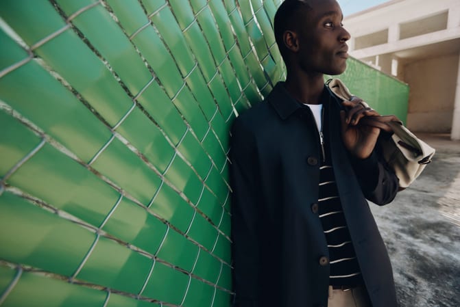 Man leaning on a green wall with a shopping bag