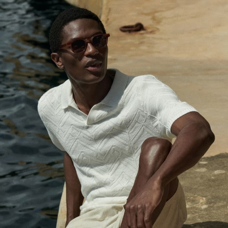 Man wearing sunglasses, a white knitted polo shirt and beige shorts. Shop tops and T-shirts.