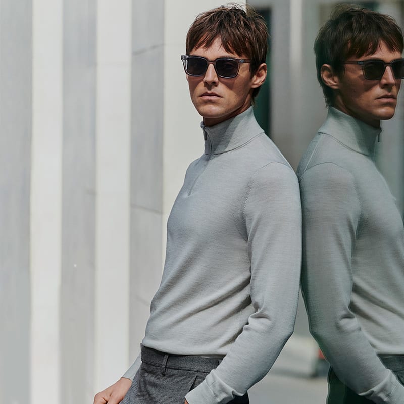 Man wearing white long-sleeved knitted polo shirt and black trousers. Shop men’s polo shirts