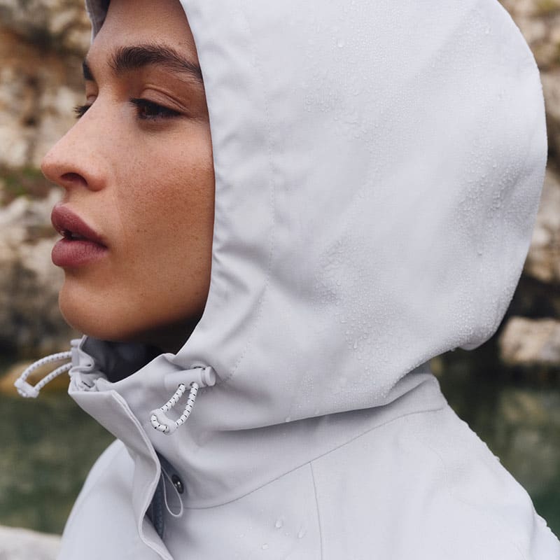 Woman wearing grey raincoat with hood. Shop women’s waterproof coats and jackets