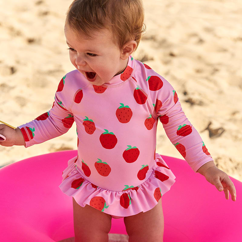 Toddler wearing strawberry print long-sleeved SPF50 swimsuit. Shop kids’ swimwear 