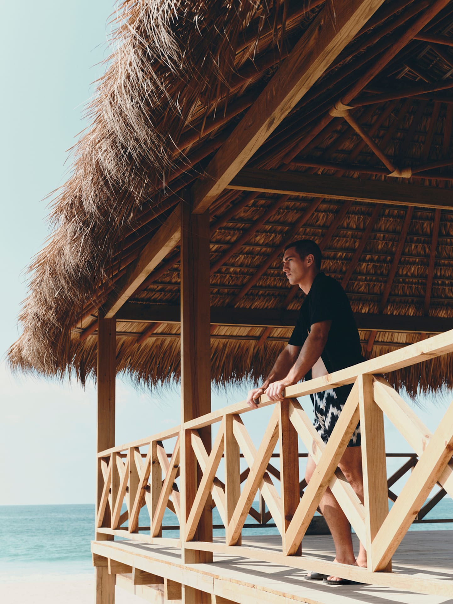Man overlooking a tropical beach from a thatched balcony