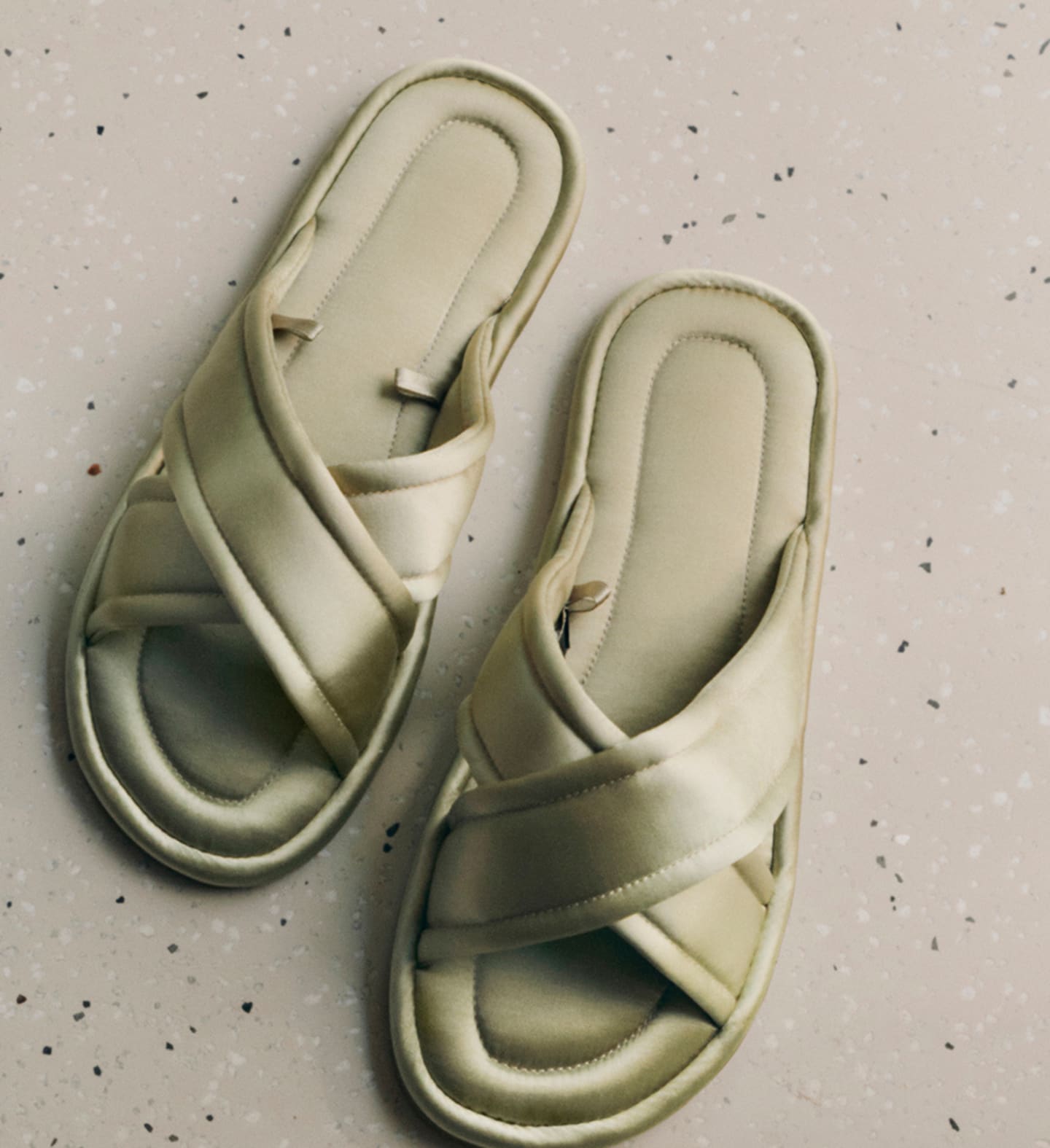 Pair of sage green cross-strap slippers on a speckled surface