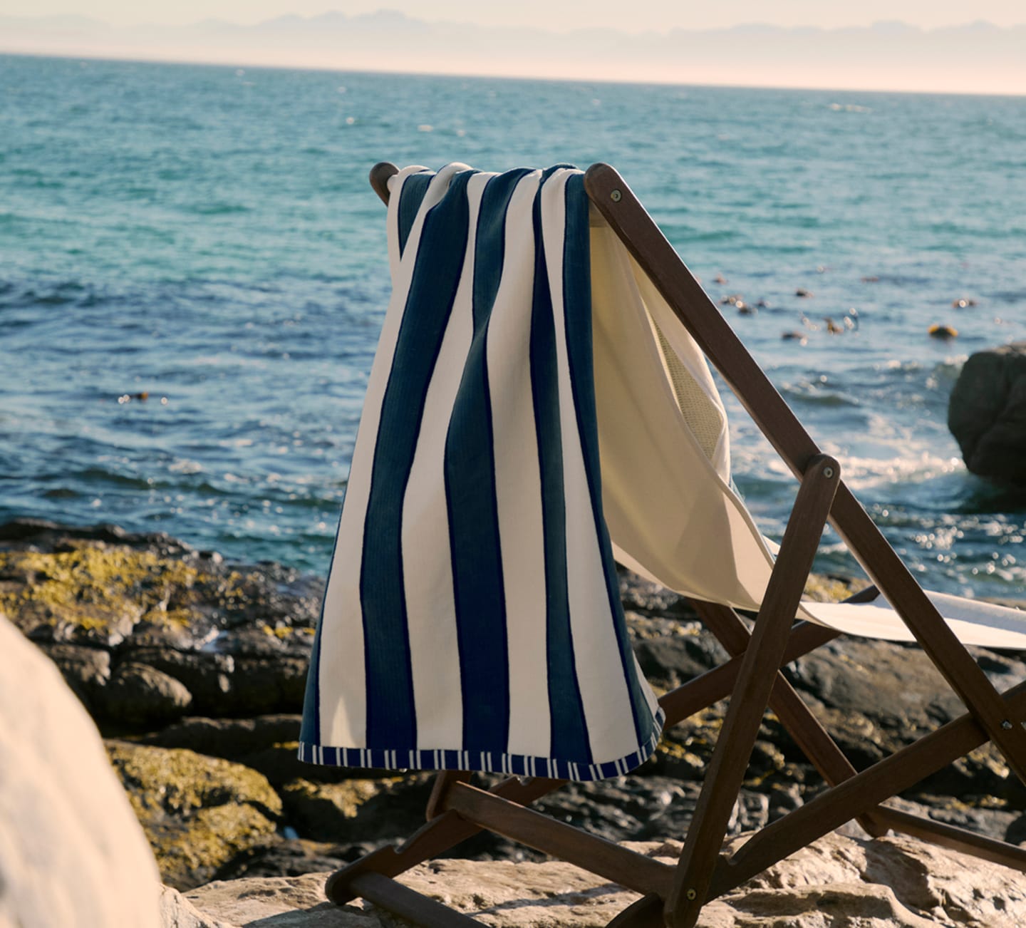 Striped beach towel draped over a wooden deck chair by the sea