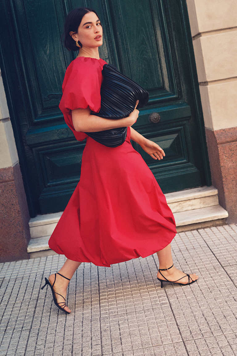 Woman in red top and red midi skirt holding black bag